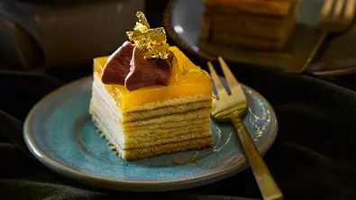 Kleine, mehrschichtige Orangen-Schoko-Baumküchlein auf einem Teller, verziert mit Schokoladencreme, Orangenspiegel und essbarem Gold. - Foto: LECKER @ Bauer Media Group