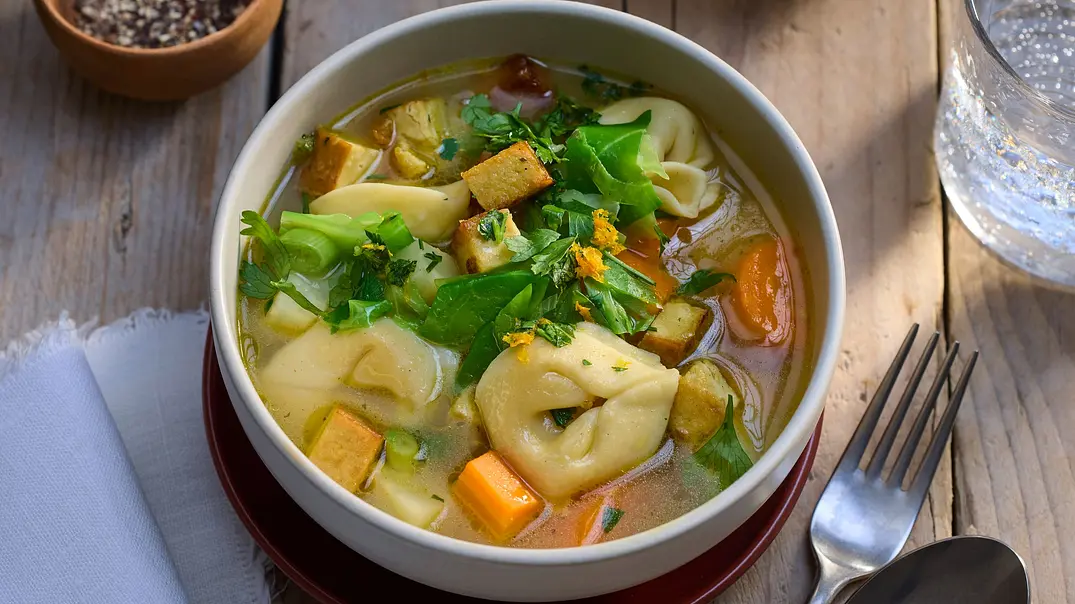 Tortellinisuppe mit herbstlichem Gemüse wie Karotten, Lauch und Tofu, serviert in einer weißen Schale auf einem Holztisch. - Foto: LECKER @ Bauer Media Group Tortellinisuppe mit herbstlichem Gemüse wie Karotten, Lauch und Tofu, serviert in einer weißen Schale auf einem Holztisch. - Foto: LECKER @ Bauer Media Group