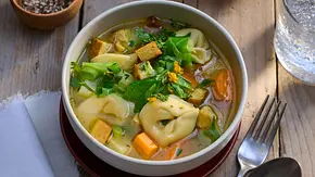 Tortellinisuppe mit herbstlichem Gemüse wie Karotten, Lauch und Tofu, serviert in einer weißen Schale auf einem Holztisch. - Foto: LECKER @ Bauer Media Group