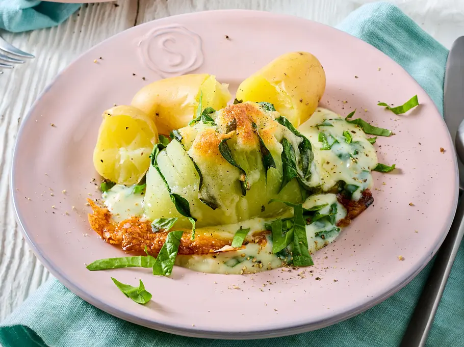 Hasselback-Kohlrabi aus dem Airfryer Rezept Hasselback-Kohlrabi mit aufgeschichteten, gerösteten Scheiben, cremiger Kräutersoße und kleinen Kartoffeln, serviert auf einem rosa Teller.
