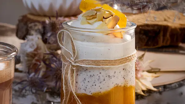 Schichtdessert aus cremigem Topfen mit Mohn und fruchtigem Aprikosenröster, angerichtet in einem hohen Glas auf rustikalem Holztisch, garniert mit gehobelten Mandeln und Orangenfilet. - Foto: LECKER @ Bauer Media Group
