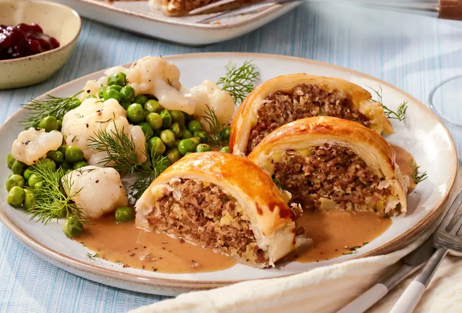 Köttbullar-Braten in Blätterteig auf Teller mit brauner Soße, Erbsen und Kartoffelpüree angerichtet