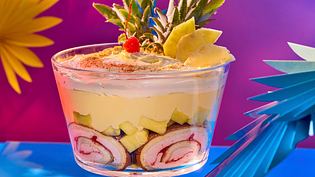 Mehrschichtiger Trifle im Glas mit feinen Biskuitrollen, Stücken von frischer Ananas, cremigen Schichten aus Piña-Colada-Creme und Sahne, getoppt mit Ananasscheiben, Ananasblättern und einer Cocktailkirsche. - Foto: LECKER @ Bauer Media Group