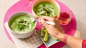 Zwei weiße Suppenschüsseln mit grüner Spargelsuppe und einer Hand, die einen Löffel reintaucht. - Foto: LECKER @ Bauer Media Group
