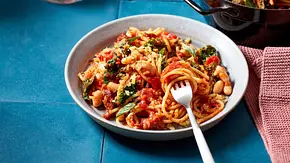 Spaghetti mit Grünkohl und weißen Bohnen in einer kräftigen Tomatensauce, serviert auf einem grauen Teller. - Foto: LECKER @ Bauer Media Group