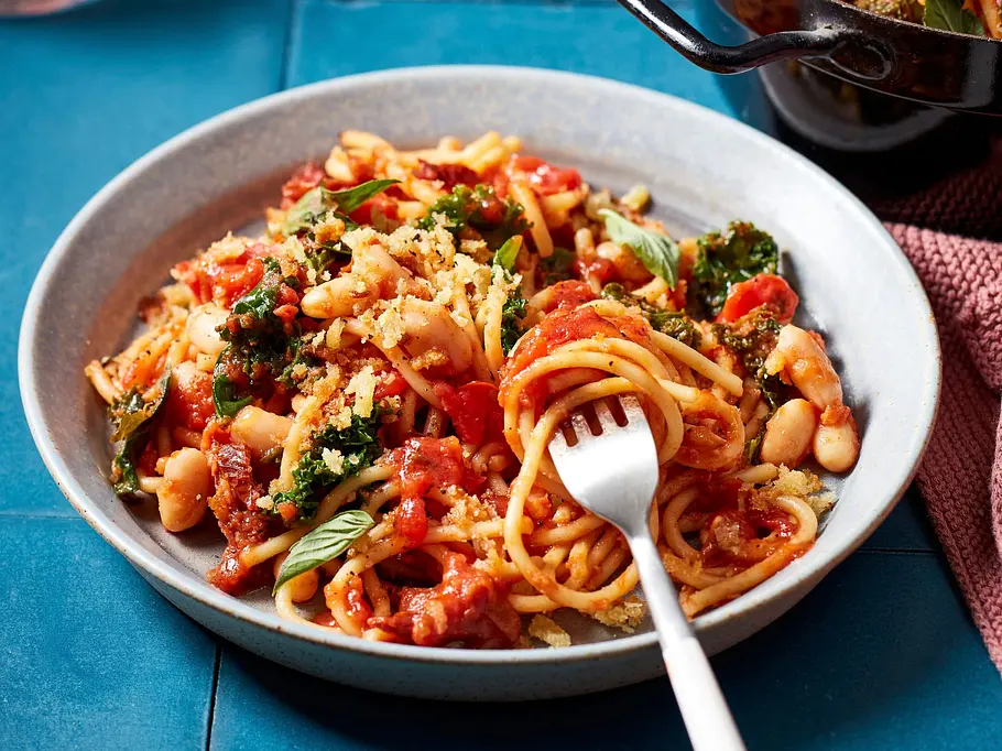 Spaghetti mit Grünkohl und weißen Bohnen in einer kräftigen Tomatensauce, serviert auf einem grauen Teller.