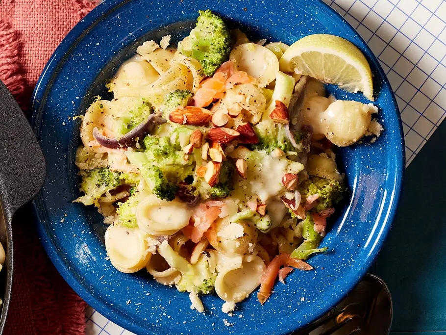 Brokkoli-Nudeln mit Lachs Rezept Orecchiette-Nudeln mit zartem Lachs, Brokkoli, roten Zwiebeln und gerösteten Mandeln in einer cremigen Sauce, serviert auf einem blauen Teller.
