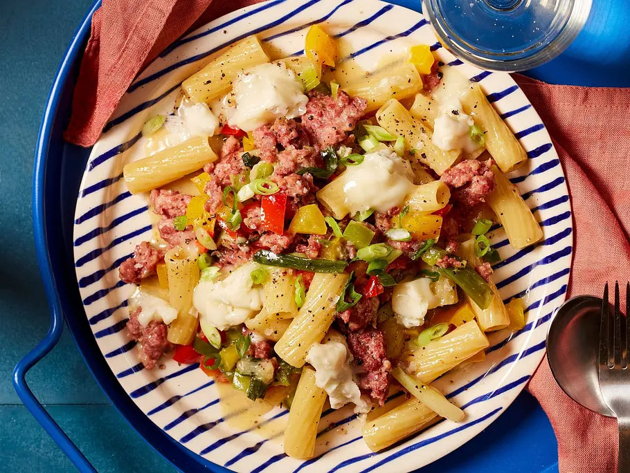 Tortiglioni-Nudeln mit gebratener Salsiccia, buntem Gemüse und cremigem Käse, angerichtet auf einem gestreiften Teller.