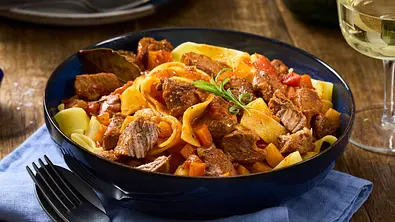 Bandnudeln mit zartem, tomatigem Lammragout, serviert in einer tiefen, dunkelblauen Schüssel auf einem blauen Untersetzer. - Foto: LECKER @ Bauer Media Group