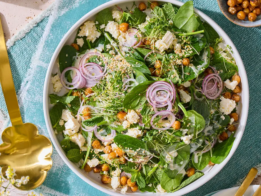 Kresse-Salat mit gerösteten Kichererbsen und Feta Frischer Kresse-Salat mit gerösteten Kichererbsen, Feta, roten Zwiebelringen und Sesam in einer weißen Schüssel auf einem türkisfarbenen Stoffset. Daneben goldenes Salatbesteck.