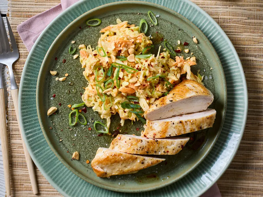 Zart gebratenes Hähnchenfilet, serviert mit einem bunten Coleslaw aus fein geschnittenem Kohl, Erdnüssen und Frühlingszwiebeln auf einem grünlichen Keramikteller.