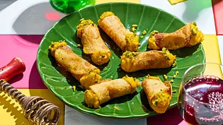 Acht herzhafte Cannoli mit goldgelber Füllung auf einem grünen, blattförmigen Teller, dazu stilvolle Weingläser mit Rotwein auf einem bunt karierten Tisch. - Foto: LECKER @ Bauer Media Group