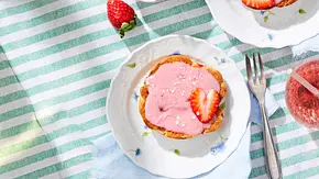 Drei Erdbeer-Amerikaner mit rosa Erdbeer-Zuckerguss, einzelnen Zuckerperlen und frischen Erdbeerscheiben, serviert auf kleinen weißen Tellern mit Blumenmotiv. - Foto: LECKER @ Bauer Media Group