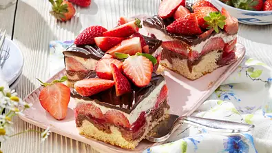 Zwei Stück Erdbeer-Donauwelle mit heller und dunkler Biskuit-Schicht, cremiger Füllung, Erdbeeren und Schokoguss, dekoriert mit frischen Erdbeeren auf einer rosa Platte. - Foto: LECKER @ Bauer Media Group