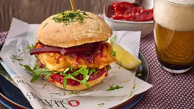 Knuspriger Backfisch-Burger im Brötchen mit Rote-Bete-Pickles und Salat auf einem Teller, dazu Zitronenspalte und ein Glas Bier mit Schaumkrone. - Foto: House of Food / StockFood Studios / Julia Hoersch