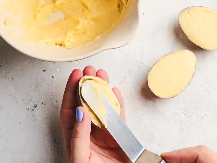 Cremige Vanillefüllung wird mit einem Messer in die Schoko-Eihälften gestrichen und glattgezogen, daneben steht eine Schüssel mit der übrigen Creme auf einer hellen Arbeitsfläche.