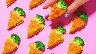 Dreieckige Cracker sind mit Frischkäse bestrichen und mit geraspelter Möhre belegt, sodass sie wie kleine Karotten aussehen; oben steckt jeweils ein Brokkoliröschen als „Karottengrün“. Eine Hand greift nach einem der Cracker vor pinkfarbenem Hintergrund. - Foto: LECKER @ Bauer Media Group Dreieckige Cracker sind mit Frischkäse bestrichen und mit geraspelter Möhre belegt, sodass sie wie kleine Karotten aussehen; oben steckt jeweils ein Brokkoliröschen als „Karottengrün“. Eine Hand greift nach einem der Cracker vor pinkfarbenem Hintergrund. - Foto: LECKER @ Bauer Media Group