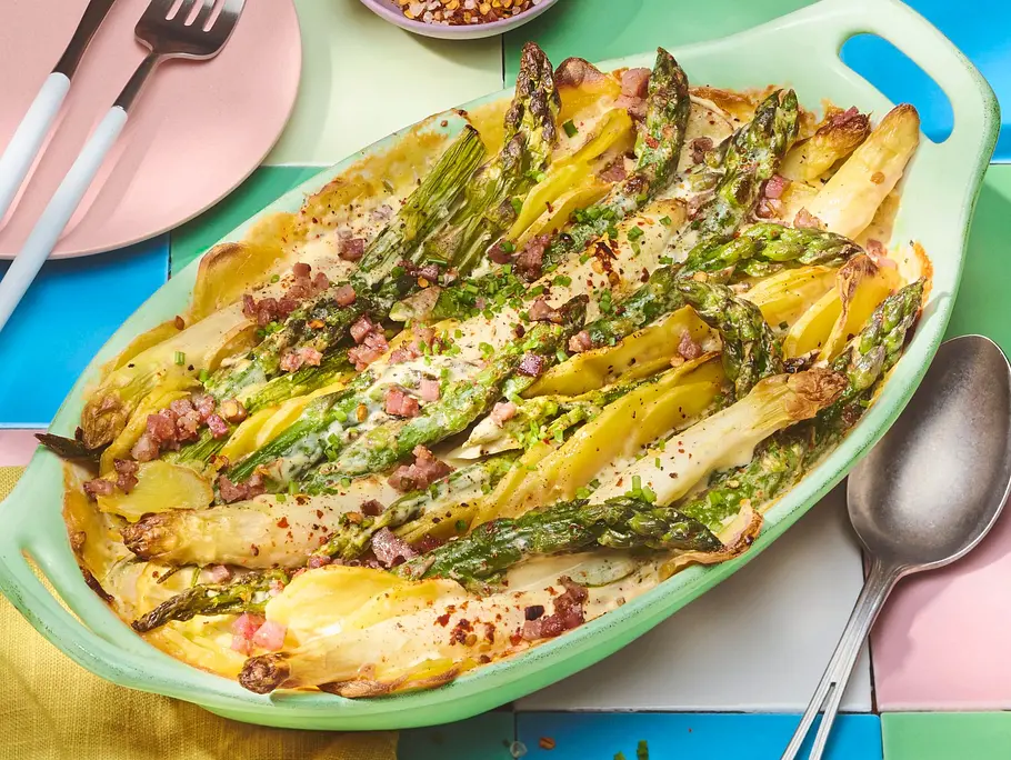 In einer Auflaufform werden Spargel und Kartoffeln als Gratin gebacken und mit Kräutern sowie Speck bestreut serviert.