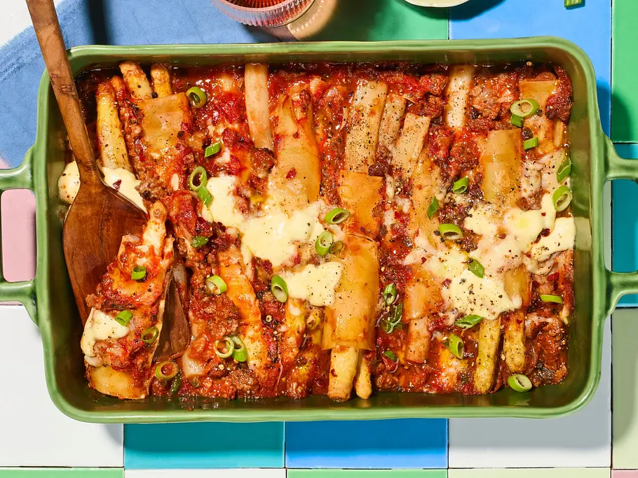 In einer Auflaufform werden Cannelloni mit Spargel in Tomatensoße überbacken und mit Frühlingszwiebeln bestreut.