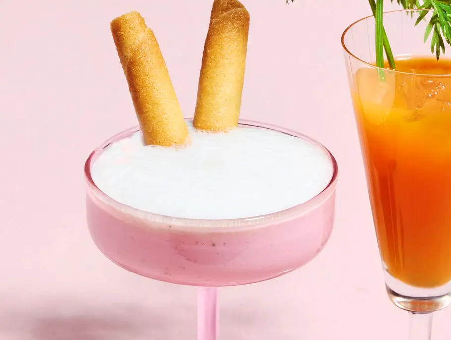 Rosa Erdbeer-Bananen-Smoothie in einem Cocktailglas, mit einer weißen Schaumschicht und zwei Keksstangen als „Hasenohren“ dekoriert – ein verspielter Oster-Smoothie.