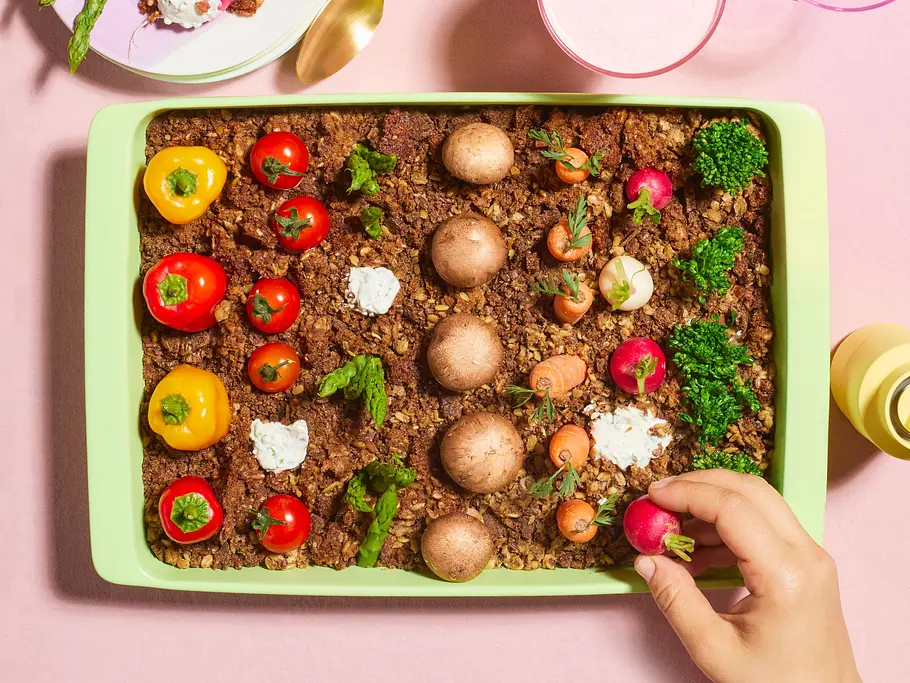 Gemüseplatte im „Dip-Beet“ angerichtet mit cremigem Dip als Erde, darauf bunte Paprika, Cherrytomaten, Radieschen, Champignons und Kräuter wie frisch gepflanztes Gemüse in einer rechteckigen Form.
