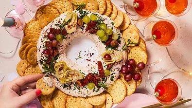 Ein runder Frischkäsekranz ist mit Kräutern, Trauben und Crackern auf einem Tisch mit Getränken angerichtet. - Foto: StockFood Studios / Meike Bergmann