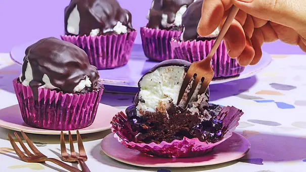 Schokokuss-Muffins ohne Zucker in lila Papierförmchen, umhüllt mit einer dicken Schokoladenschicht, auf kleinen Tellern angerichtet, ein Muffin wird mit einer Gabel angeschnitten. - Foto: LECKER @ Bauer Media Group
