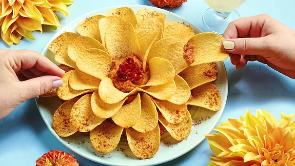 Kartoffelchips in Form einer Blüte auf einem weißen Teller, in der Mitte ein Dip mit Chili, serviert auf blauer Unterlage. - Foto: LECKER @ Bauer Media Group
