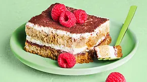 Stück Himbeer-Tiramisu mit Kakaopulver bestäubt und frischen Himbeeren garniert, serviert auf einem grünen Teller mit kleiner Gabel - Foto: LECKER @ Bauer Media Group