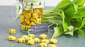 Kleine, gebackene Bärlauchkekse in Blümchenform, dekorativ in ein Glas mit grünem Stoffdeckel gefüllt, daneben frischer Bärlauch auf einer dunklen Oberfläche. - Foto: LECKER @ Bauer Media Group Kleine, gebackene Bärlauchkekse in Blümchenform, dekorativ in ein Glas mit grünem Stoffdeckel gefüllt, daneben frischer Bärlauch auf einer dunklen Oberfläche. - Foto: LECKER @ Bauer Media Group