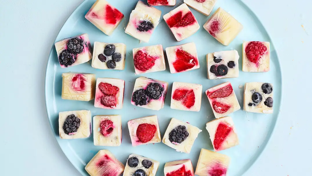 Verschiedene gefrorene Frozen-Yogurt-Würfel mit bunten Beeren auf einem runden, hellblauen Teller. - Foto:  House of Food / StockFood Studios / Meike Bergmann