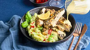 Knuspriges Low-Carb-Tonkatsu auf cremigem Avocado-Blumenkohl-Mash in einer dunklen Schale, garniert mit Zitronenscheibe, Chili und frischem Basilikum; daneben goldenes Besteck auf einem blauen Stoff. - Foto: LECKER @ Bauer Media Group