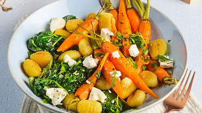 Gebratene Gnocchi mit jungen Möhren, frischem Blattspinat und kleinen Stücken Ziegenkäse auf einem hellen Teller, dazu eine gestreifte Stoffserviette als Unterlage. - Foto: StockFood Studios / Meike Bergmann