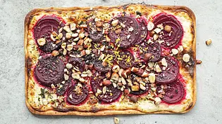 Rechteckiger Flammkuchen auf heller Steinplatte, belegt mit dünnen Scheiben Rote Bete, gehackten Nüssen, frischem Dill und Zitronenzesten. - Foto: Simone Neufing/MOE‘S QUICK & EASY FOOD
