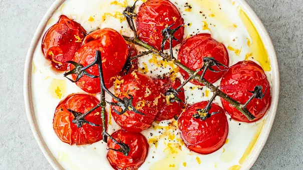 Cremig aufgeschlagener Feta serviert in einer flachen, hellen Schale, getoppt mit gerösteten Kirschtomaten am Zweig, verfeinert mit Olivenöl und Zitronenzesten. - Foto: Simone Neufing/MOE‘S QUICK & EASY FOOD