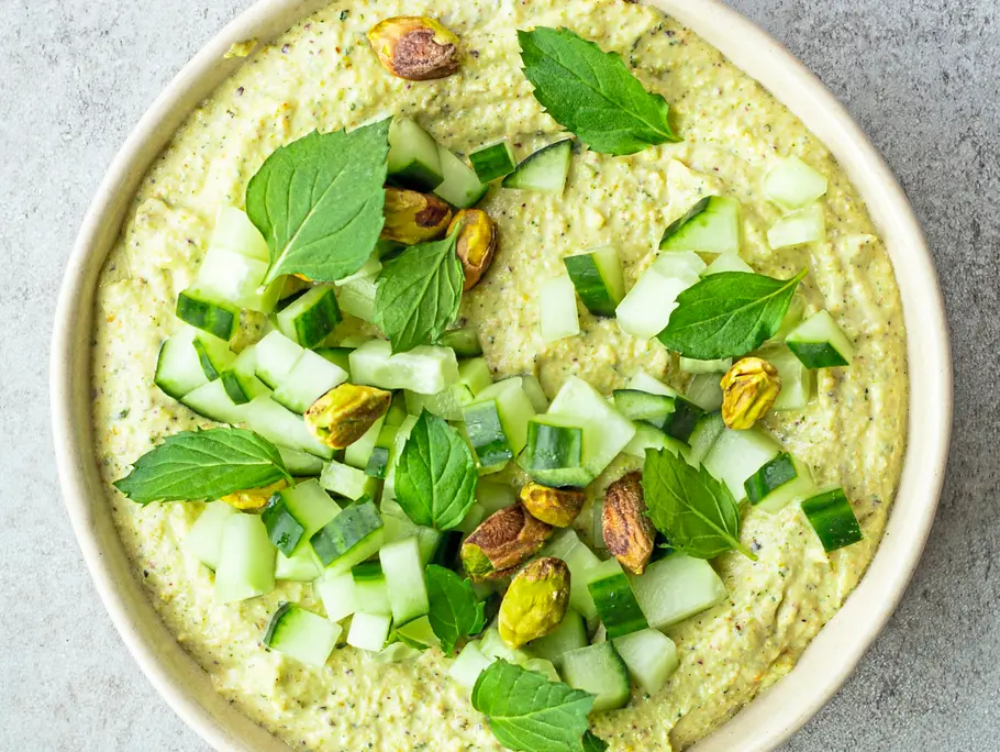 Cremiger, aufgeschlagener Feta mit Pistazien und einem Hauch Honig in einer hellen Schale, garniert mit frischer Gurke, ganzen Pistazien und Minzblättern.