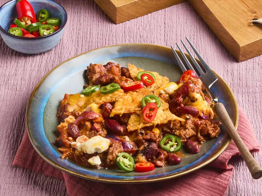 Chili con Carne vom Blech Rezept Chili con Carne mit Bohnen, Mais, geschmolzenem Käse und knusprigen Tortilla-Chips auf einem Teller.