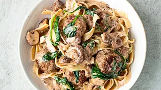 Bandnudeln mit cremiger Pilzsauce, gebratenen Köttbullar und frischem Spinat, serviert in einer weißen Schale. - Foto: Simone Neufing / MOES QUICK & EASY FOOD