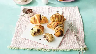 Luftige Schokoladenhörnchen mit Schokofüllung und Schokoladenstreifen auf einer weißen Platte, angerichtet auf einem rosa Tuch. - Foto: StockFood Studios/Maria Brinkop Luftige Schokoladenhörnchen mit Schokofüllung und Schokoladenstreifen auf einer weißen Platte, angerichtet auf einem rosa Tuch. - Foto: StockFood Studios/Maria Brinkop