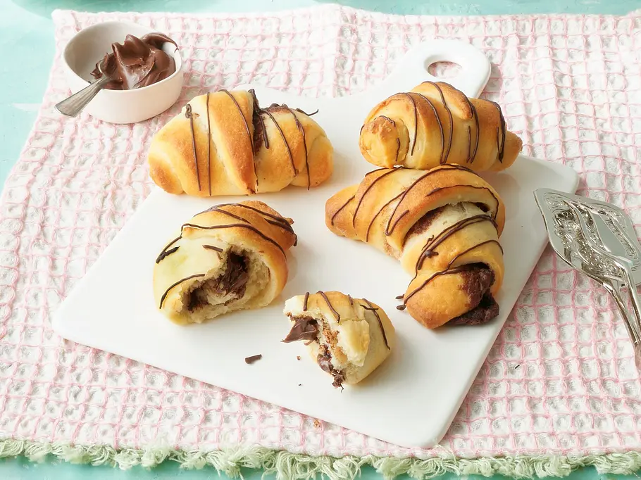 Schoko-Hörnchen aus dem Airfryer Luftige Schokoladenhörnchen mit Schokofüllung und Schokoladenstreifen auf einer weißen Platte, angerichtet auf einem rosa Tuch.