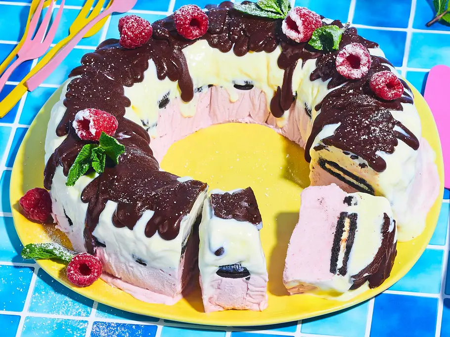 Frozen Fürst-Pückler-Kranz mit Oreos Gefrorener Fürst-Pückler-Kranz mit Schoko- und Vanillesahne, Oreo-Keksstücken und Himbeeren, dekoriert mit Minzblättern, serviert auf einem gelben Teller.