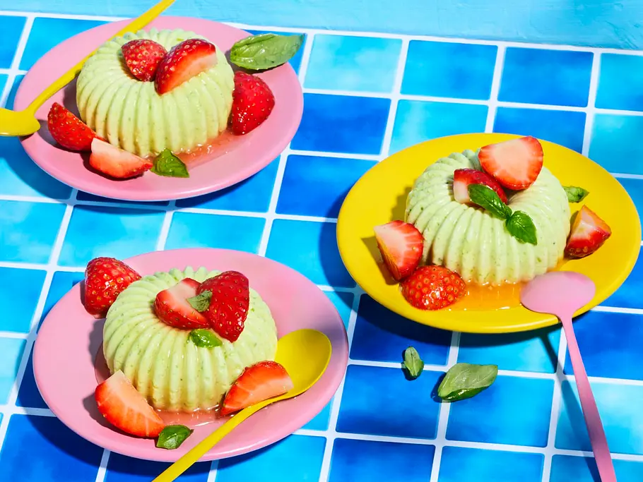 Gin-Basil-Smash-Semifreddo Gin-Basilikum-Semifreddo in kleinen Gugelhupf-Formen, serviert auf pinken und gelben Tellern, dekoriert mit frischen Erdbeeren, Basilikumblättern und bunten Löffeln.