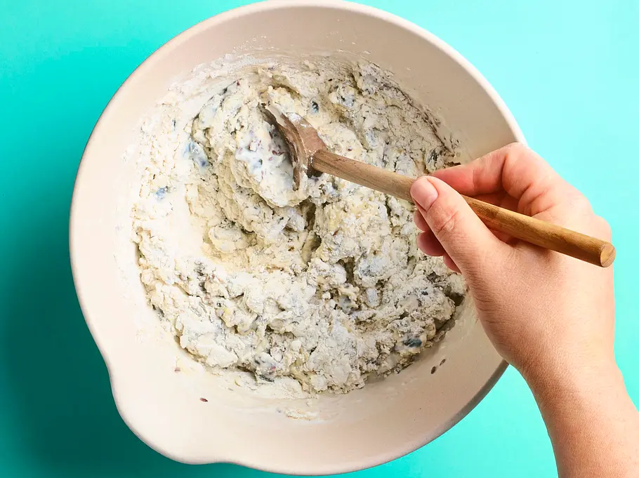Kerniges Brot im Glas Helle Rührschüssel mit bereits verrührtem, kernigem Brotteig, der mit einem Holzlöffel von Hand gemischt wird.