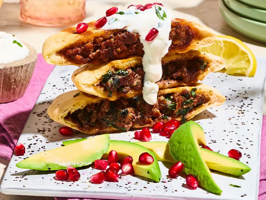 Dreierlei gefüllte Arayes, belegt mit Minzdip und Granatapfelkernen, angerichtet auf einem marmorierten Teller mit Avocado-Stücken, dazu ein Schälchen Minzdip.
