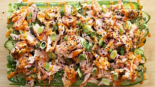 Gestreifter Sushi-Reis mit Gurkenscheiben, darauf zarter Lachs, Sesam, Frühlingszwiebeln und Sriracha-Sauce, angerichtet auf einem Holzbrett. - Foto: Simone Neufing/MOE‘S QUICK & EASY FOOD Gestreifter Sushi-Reis mit Gurkenscheiben, darauf zarter Lachs, Sesam, Frühlingszwiebeln und Sriracha-Sauce, angerichtet auf einem Holzbrett. - Foto: Simone Neufing/MOE‘S QUICK & EASY FOOD