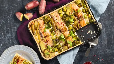 Herzhafte Lachs-Quiche mit Kartoffelscheiben und Rosenkohl in einer eckigen Backform auf einem dunklen Untergrund, dazu ein Stück auf einem hellen, geriffelten Teller. - Foto: StockFood Studios/Meike Bergmann Herzhafte Lachs-Quiche mit Kartoffelscheiben und Rosenkohl in einer eckigen Backform auf einem dunklen Untergrund, dazu ein Stück auf einem hellen, geriffelten Teller. - Foto: StockFood Studios/Meike Bergmann