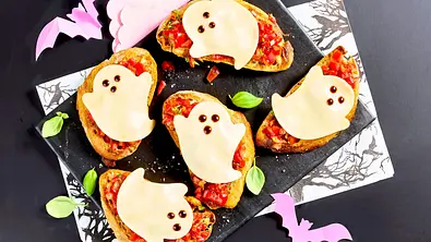Vier Scheiben Bruschetta mit Tomatenbelag, jeweils mit einer Mozzarella-Scheibe in Geisterform belegt und auf einer schwarzen Servierplatte angerichtet, dekoriert mit frischem Basilikum. - Foto: StockFood Studios/Meike Bergmann Vier Scheiben Bruschetta mit Tomatenbelag, jeweils mit einer Mozzarella-Scheibe in Geisterform belegt und auf einer schwarzen Servierplatte angerichtet, dekoriert mit frischem Basilikum. - Foto: StockFood Studios/Meike Bergmann