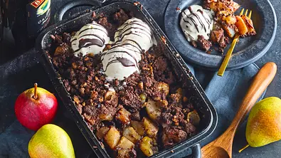 Birnencrumble mit Eis und Schokosoße steht in einer Backform neben einem Dessertteller, Birnen, Holzlöffel und einer Baileys-Flasche. - Foto: StockFood Studios / Meike Bergmann Birnencrumble mit Eis und Schokosoße steht in einer Backform neben einem Dessertteller, Birnen, Holzlöffel und einer Baileys-Flasche. - Foto: StockFood Studios / Meike Bergmann