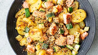 Bratkartoffeln mit zarten Lachsstücken und gebratener Zucchini, bestreut mit Sesam, serviert in einer dunklen Pfanne. - Foto: Simone Neufing/MOE‘S QUICK & EASY FOOD Bratkartoffeln mit zarten Lachsstücken und gebratener Zucchini, bestreut mit Sesam, serviert in einer dunklen Pfanne. - Foto: Simone Neufing/MOE‘S QUICK & EASY FOOD