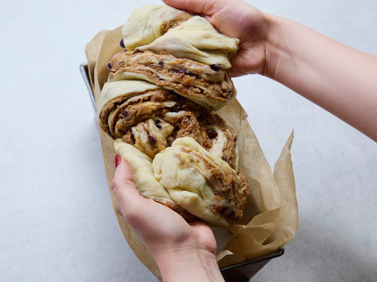 Spekulatius-Karamell-Babka Rezept Hände legen locker zu einer Kordel gedrehte, gefüllte Teigstränge für die Spekulatius-Karamell-Babka vorsichtig in eine mit Backpapier ausgelegte Kastenform.